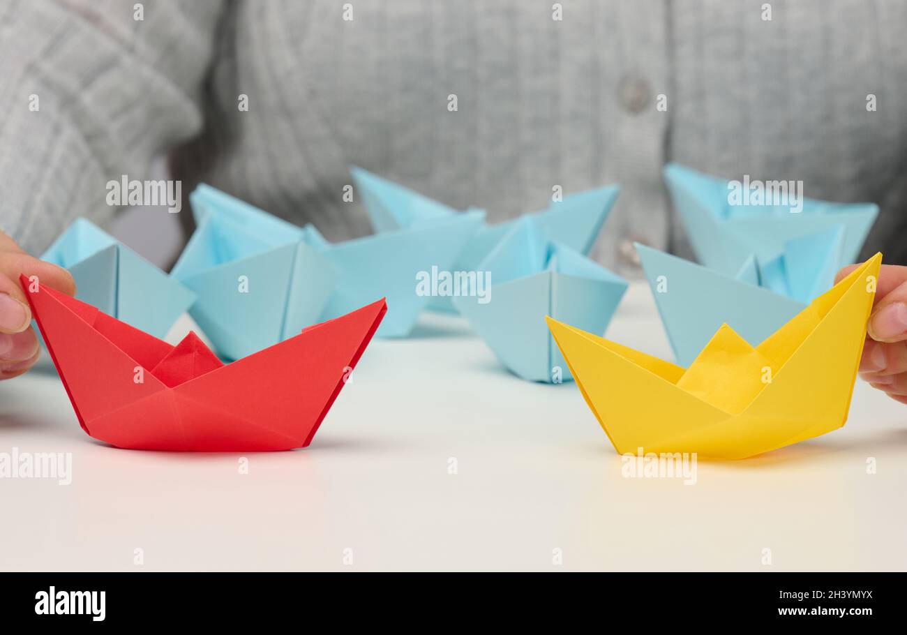 Les femmes tiennent les bateaux en papier rouge et jaune sur une table blanche.Confrontation, suivre un dirigeant fort, Dailog Banque D'Images