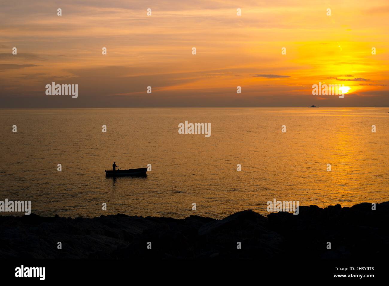 Un pêcheur sur un bateau près de la rive sur fond d'un coucher de soleil doré. Banque D'Images