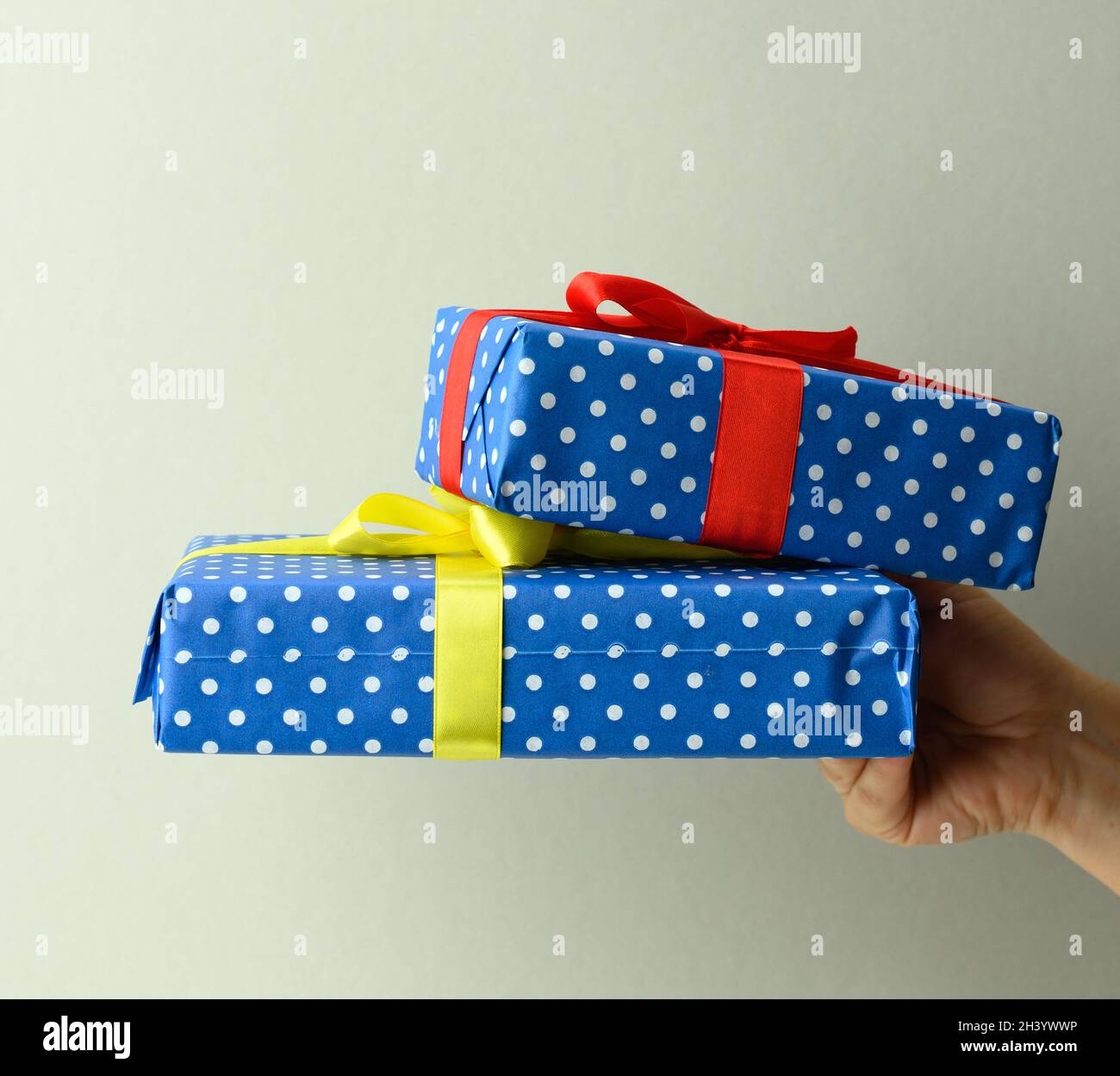 Main féminine tenant une pile de boîtes cadeau attaché avec ruban de soie sur un fond gris, surprise et gagner Banque D'Images