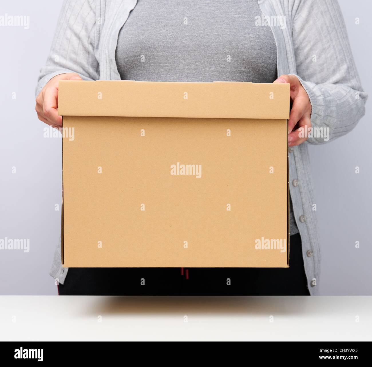 Femme en chevets gris et tient une boîte brune sur un fond blanc, déplaçant, envoyant et livrant des marchandises Banque D'Images