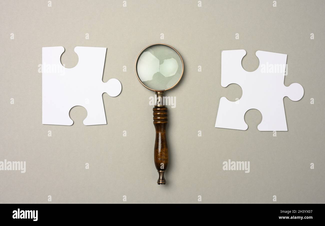 Puzzles blancs autour d'une loupe sur fond gris. Concept de recherche de personnes talentueuses, recrutement du personnel, Banque D'Images