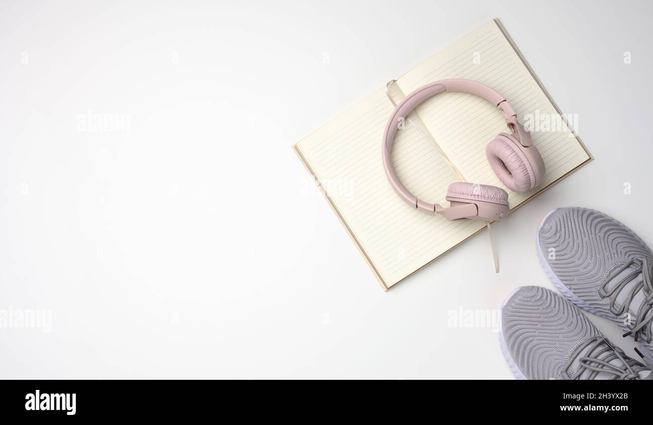 Casque sans fil rose, une paire de baskets et un bloc-notes sur fond blanc, vue du dessus.Vêtements pour femmes Banque D'Images