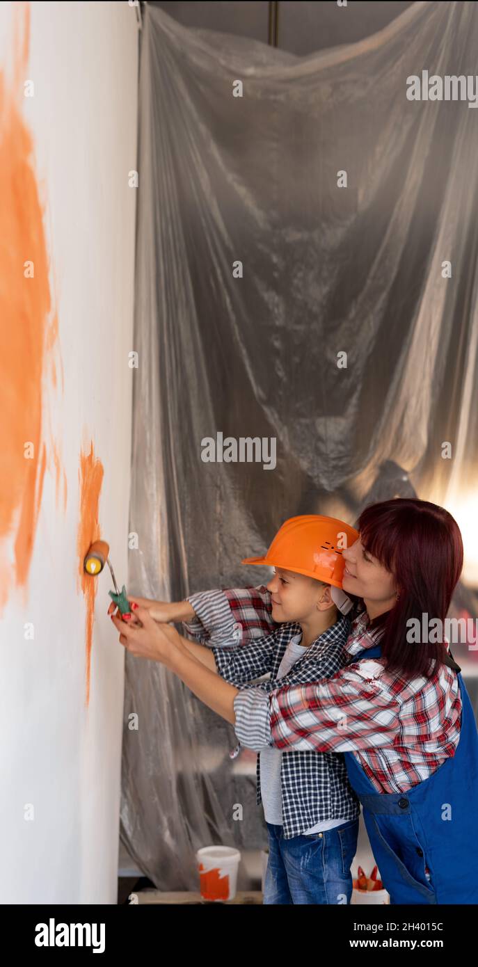 Maman et son fils peignent un mur dans une nouvelle maison.Une femme enseigne à un enfant à peindre avec un rouleau lors de la réparation d'un appartement.Concept de rénovation. Banque D'Images