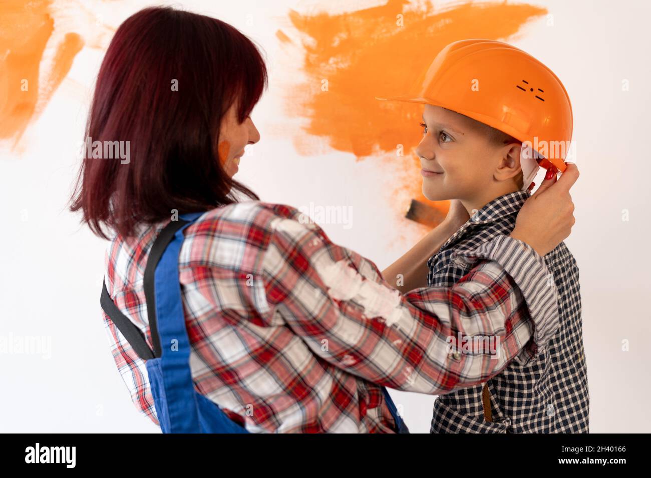 Réparer.Bonne famille maman et fils dans casque peinture maison mur intérieur.Peignez le mur à l'orange.Portrait d'une femme avec un enfant, réparateur. Banque D'Images