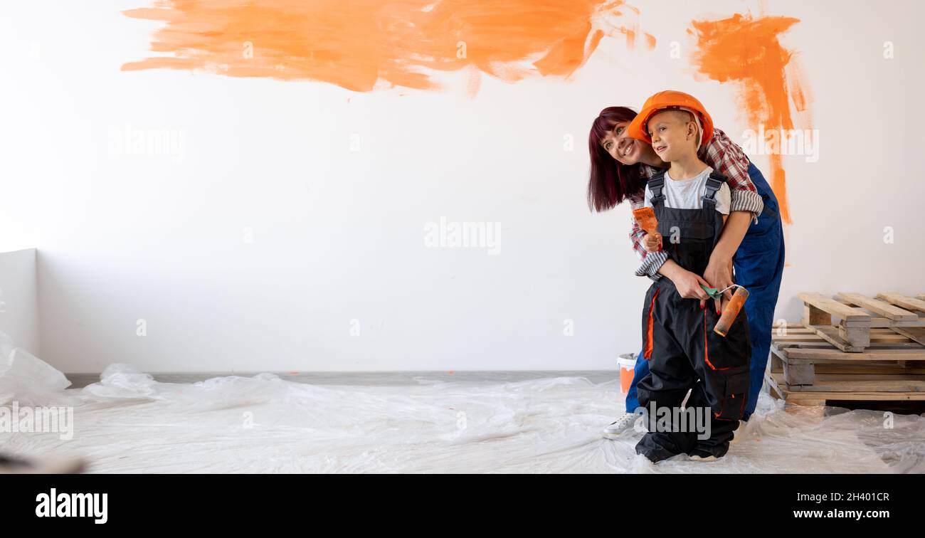 Réparations à domicile.Une maman et un fils heureux de famille ont peint le mur à l'orange.Peinture murale.Rénovation ou rénovation de la chambre.Femme et enfant dans un casque Banque D'Images