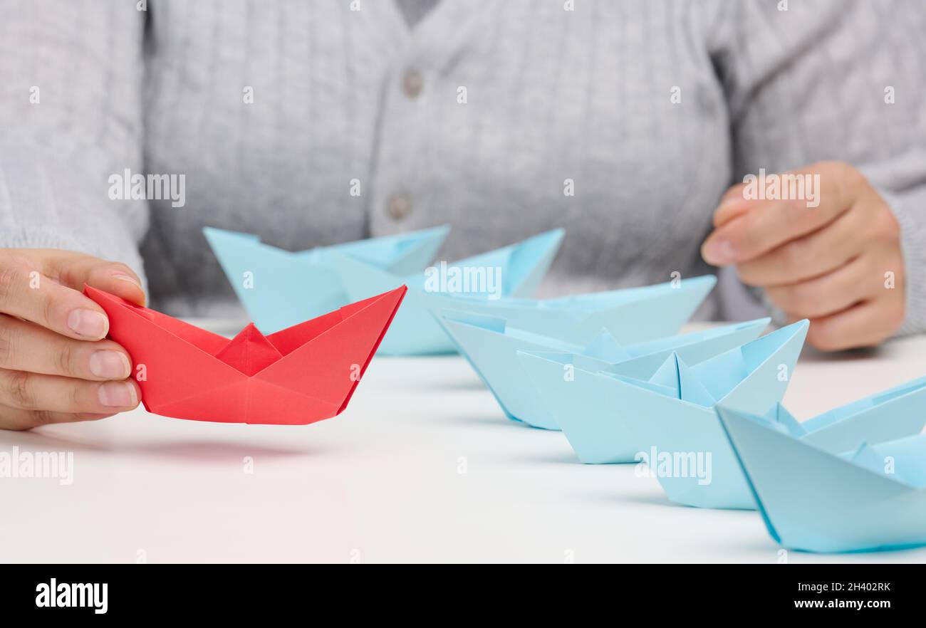 Un groupe de bateaux en papier bleu suit un bateau res devant une table blanche.Le concept d'un leader fort et charismatique dans une équipe Banque D'Images
