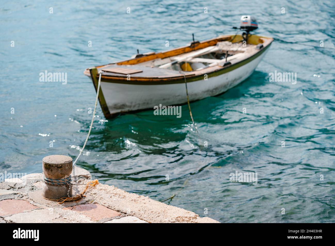 Un vieux bollard de mer en pierre sur la jetée, avec un bateau de pêche en bois attaché. Banque D'Images