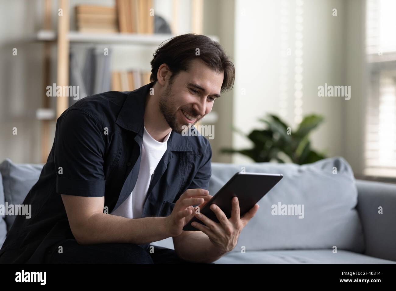 Joyeux jeune homme beau utilisant une tablette d'ordinateur numérique. Banque D'Images