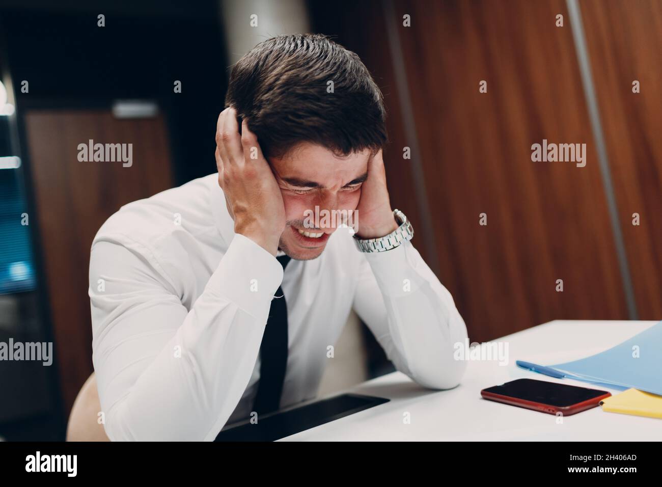 Un jeune homme d'affaires triste s'assoit et tient la tête avec ses mains à la table de bureau.Les gens d'affaires maux de tête en crise et dépression après Banque D'Images