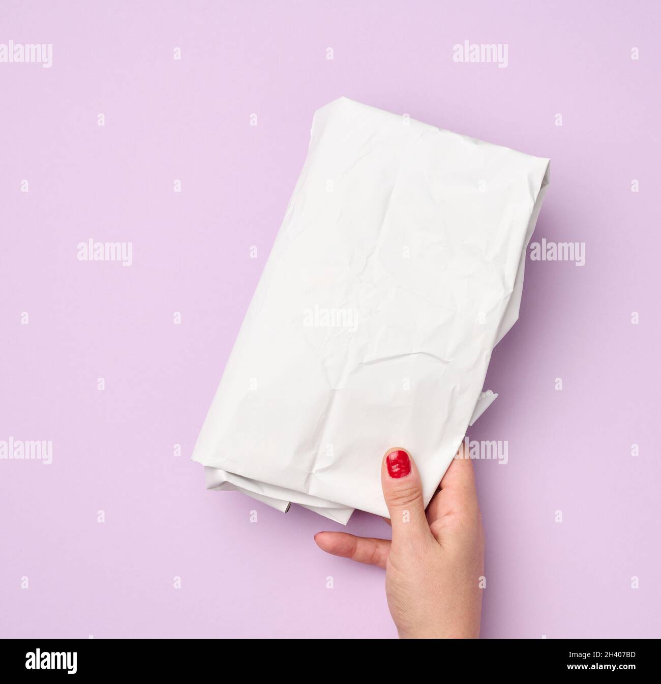 Main tenir l'emballage plié papier blanc froissé sur fond violet Banque D'Images