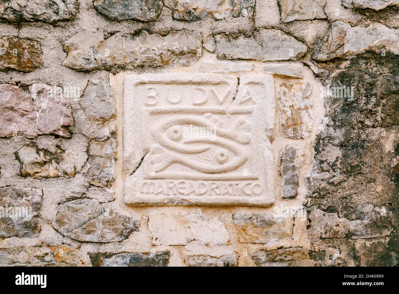 Un vieux mur en pierre avec un bas-relief appliqué avec l'inscription BUDVA mare adriatico et deux poissons. Banque D'Images