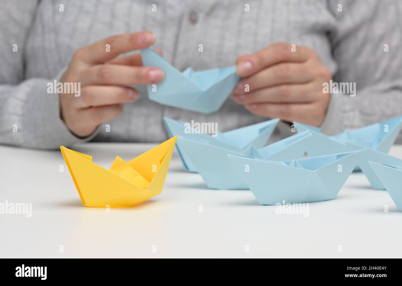 Groupe de bateaux en papier bleu suit un bateau jaune devant un fond blanc.Le concept d'un leader fort et charismatique Banque D'Images