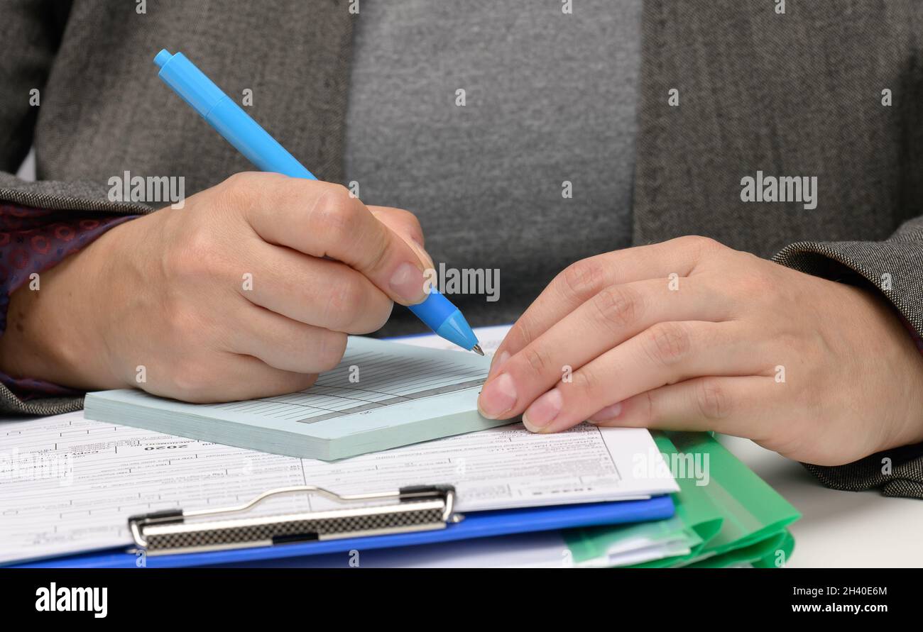 Femme d'apparence caucasienne assis dans des vêtements gris à une table blanche et signe des documents avec un stylo en métal.Homme d'affaires au travail, s Banque D'Images