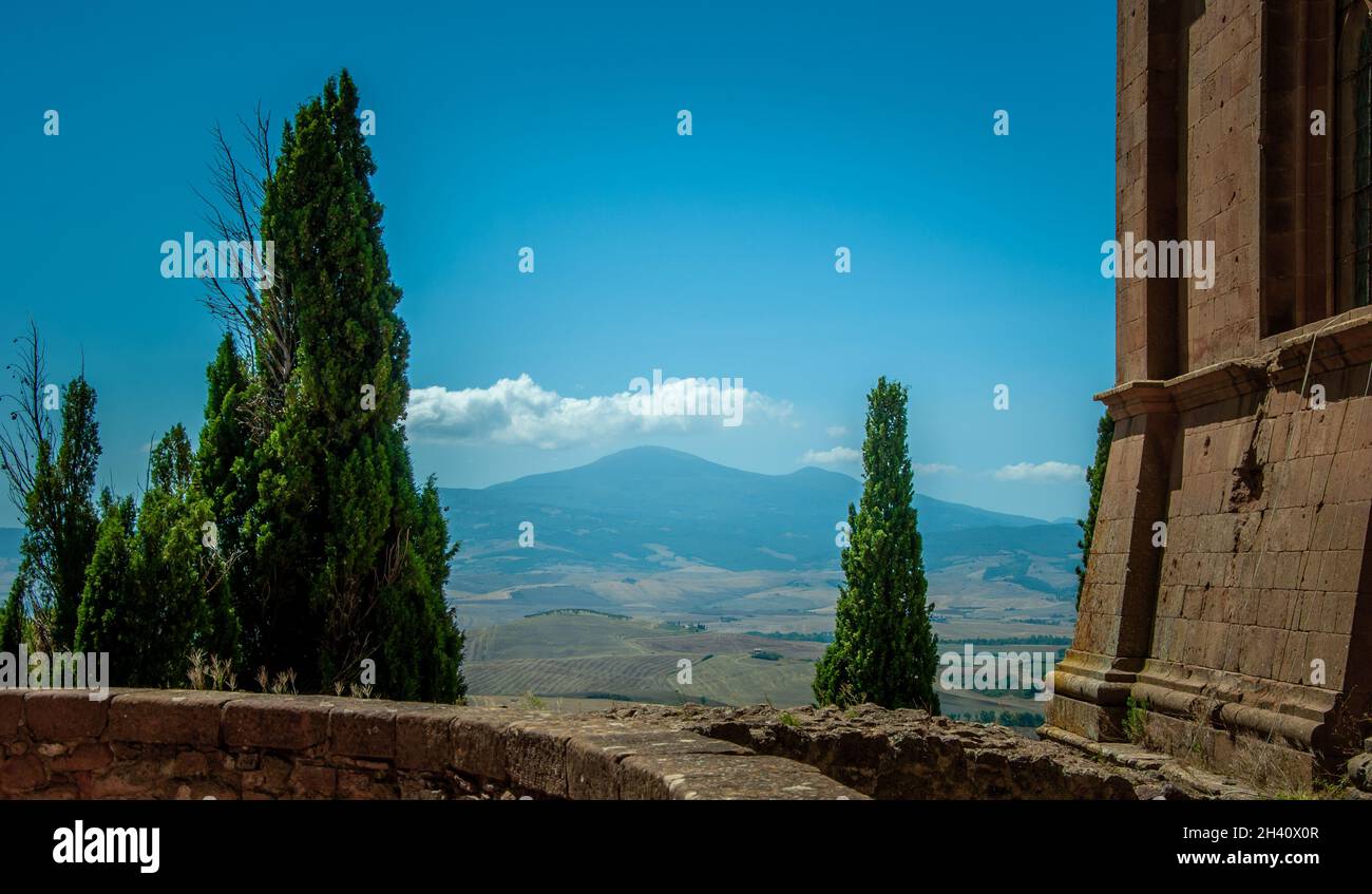 Monte Amiata dans le ciel bleu de Montepulciano avec de petits nuages blancs au sommet, en été avec cyprès et mur d'église au premier plan. Banque D'Images