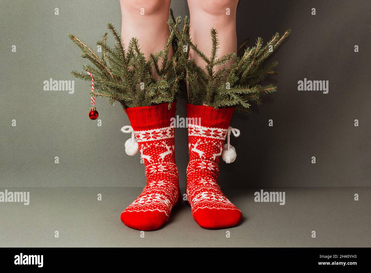 Pattes de femme en chaussettes rouges en laine avec ornements et branches de sapin minimaliste décorées sur fond vert.Concept d'arbre de Noël créatif.Bonne Christma Banque D'Images