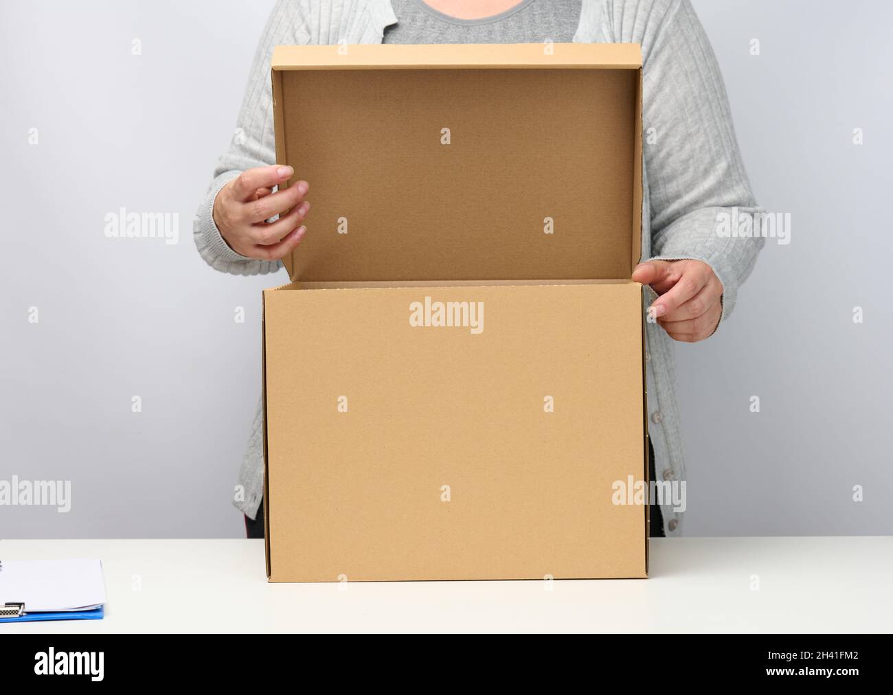 Femme dans les supports de vêtements gris et tient la boîte brune ouverte sur un fond blanc, déplaçant, envoyant et livrant des marchandises Banque D'Images