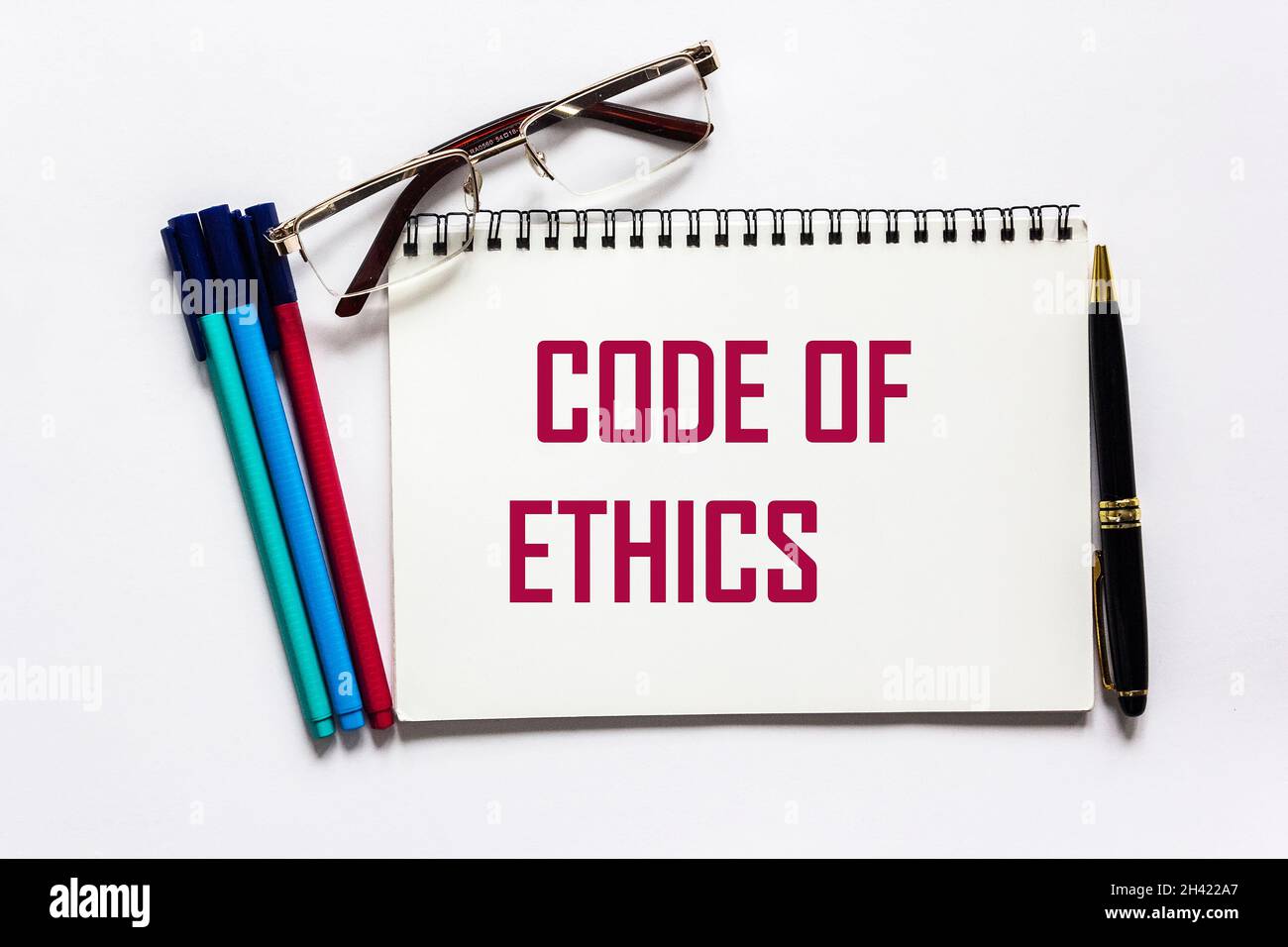 Code d'éthique écrit sur un bloc-notes et un fond blanc, près des stylos-feutres, un stylo et des lunettes. Banque D'Images