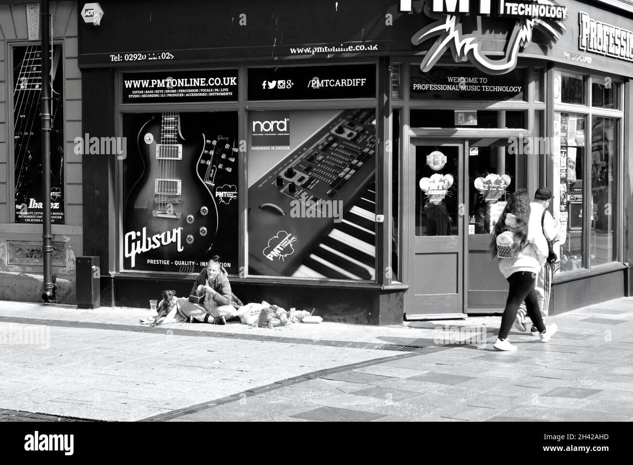 Cardiff, pays de Galles, juillet 31 2021 : image monochrome des acheteurs qui marchent devant une jeune femme sans abri assise sur le trottoir du centre-ville de Cardiff. Banque D'Images Cardiff, pays de Galles, juillet 31 2021 : image monochrome des acheteurs qui marchent devant une jeune femme sans abri assise sur le trottoir du centre-ville de Cardiff. Banque D'Images