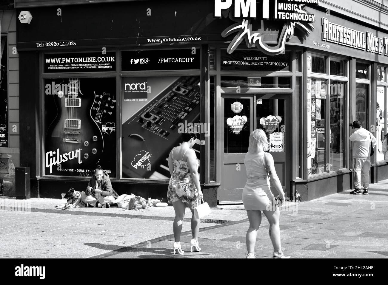 Cardiff, pays de Galles, juillet 31 2021 : image monochrome des acheteurs qui marchent devant une jeune femme sans abri assise sur le trottoir du centre-ville de Cardiff. Banque D'Images Cardiff, pays de Galles, juillet 31 2021 : image monochrome des acheteurs qui marchent devant une jeune femme sans abri assise sur le trottoir du centre-ville de Cardiff. Banque D'Images