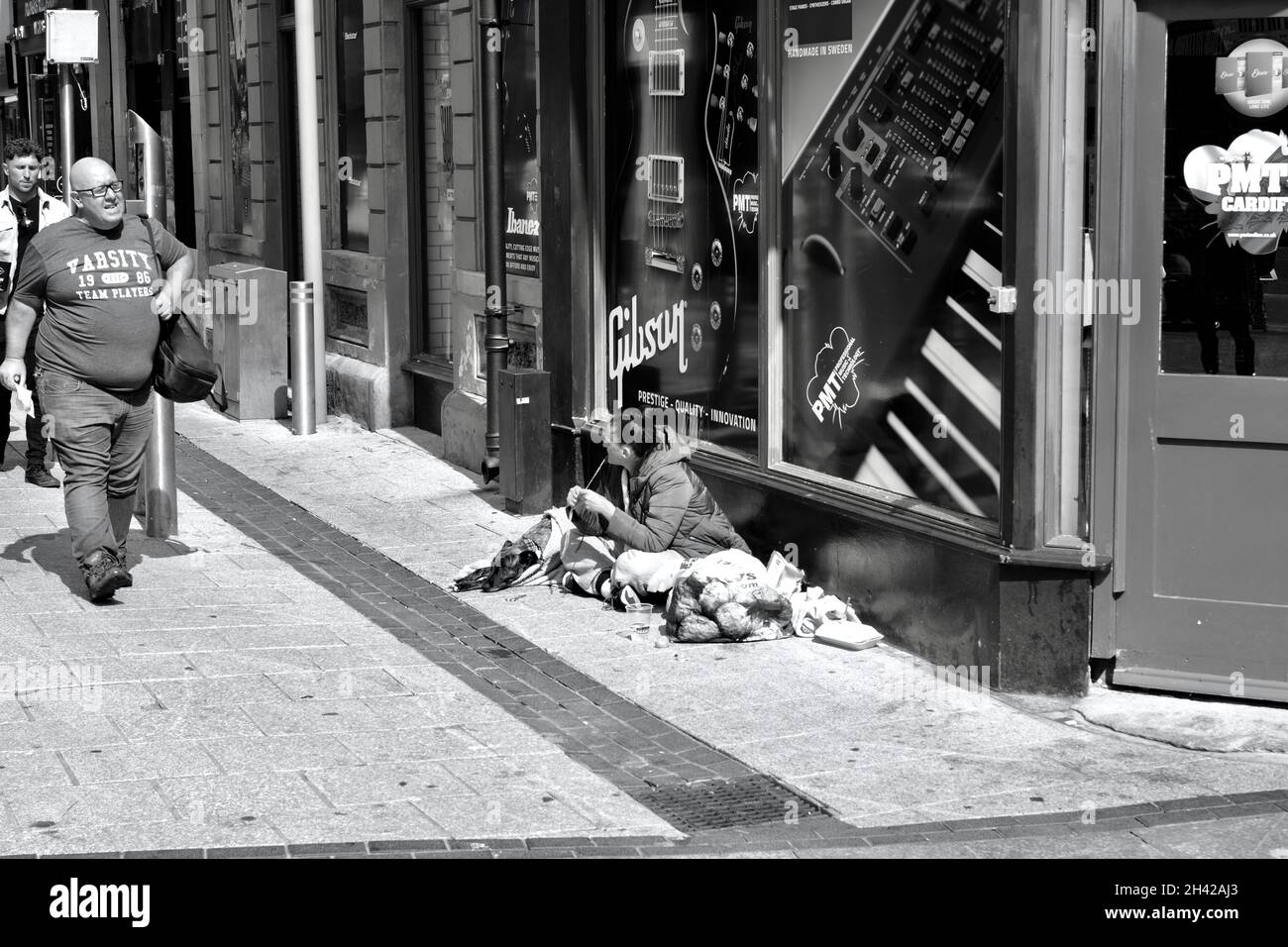 Cardiff, pays de Galles, juillet 31 2021 : image monochrome des acheteurs qui marchent devant une jeune femme sans abri assise sur le trottoir du centre-ville de Cardiff. Banque D'Images Cardiff, pays de Galles, juillet 31 2021 : image monochrome des acheteurs qui marchent devant une jeune femme sans abri assise sur le trottoir du centre-ville de Cardiff. Banque D'Images