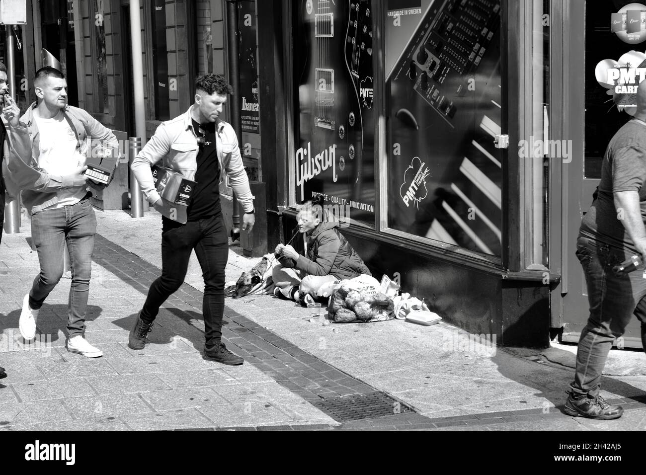 Cardiff, pays de Galles, juillet 31 2021 : image monochrome des acheteurs qui marchent devant une jeune femme sans abri assise sur le trottoir du centre-ville de Cardiff. Banque D'Images Cardiff, pays de Galles, juillet 31 2021 : image monochrome des acheteurs qui marchent devant une jeune femme sans abri assise sur le trottoir du centre-ville de Cardiff. Banque D'Images