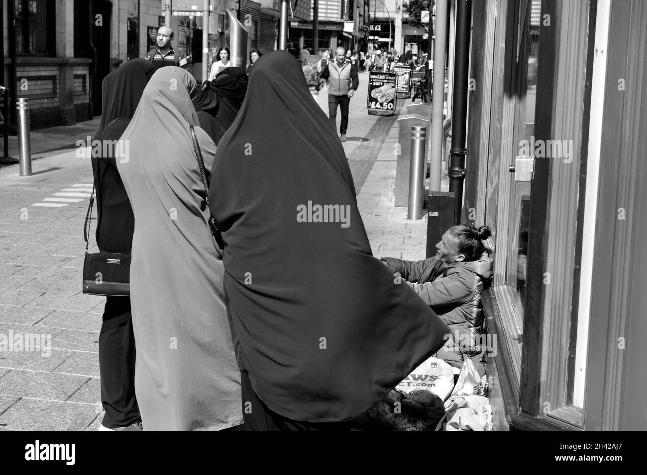 Cardiff, pays de Galles le 31 2021 juillet : une jeune femme sans domicile assise sur le trottoir du centre-ville de Cardiff.Un groupe de femmes asiatiques dans les hijabs s'arrêtent de parler Banque D'Images Cardiff, pays de Galles le 31 2021 juillet : une jeune femme sans domicile assise sur le trottoir du centre-ville de Cardiff.Un groupe de femmes asiatiques dans les hijabs s'arrêtent de parler Banque D'Images