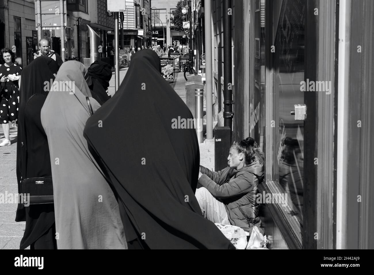 Cardiff, pays de Galles le 31 2021 juillet : une jeune femme sans domicile assise sur le trottoir du centre-ville de Cardiff.Un groupe de femmes asiatiques dans les hijabs s'arrêtent de parler Banque D'Images Cardiff, pays de Galles le 31 2021 juillet : une jeune femme sans domicile assise sur le trottoir du centre-ville de Cardiff.Un groupe de femmes asiatiques dans les hijabs s'arrêtent de parler Banque D'Images