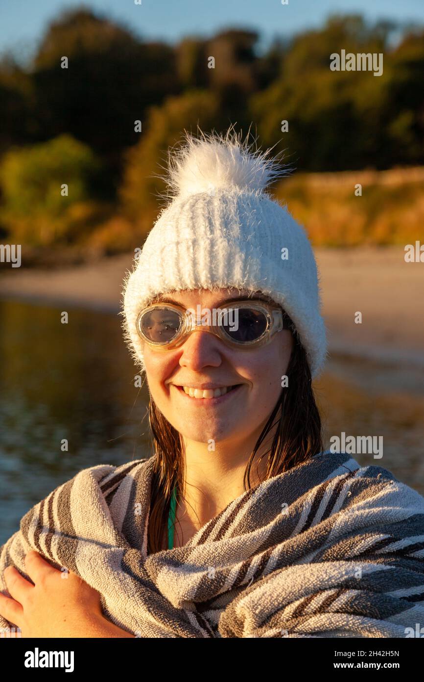 Une femme portant un chapeau laineux et des lunettes de natation enveloppées dans une serviette après une baignade d'eau froide matinale. Banque D'Images