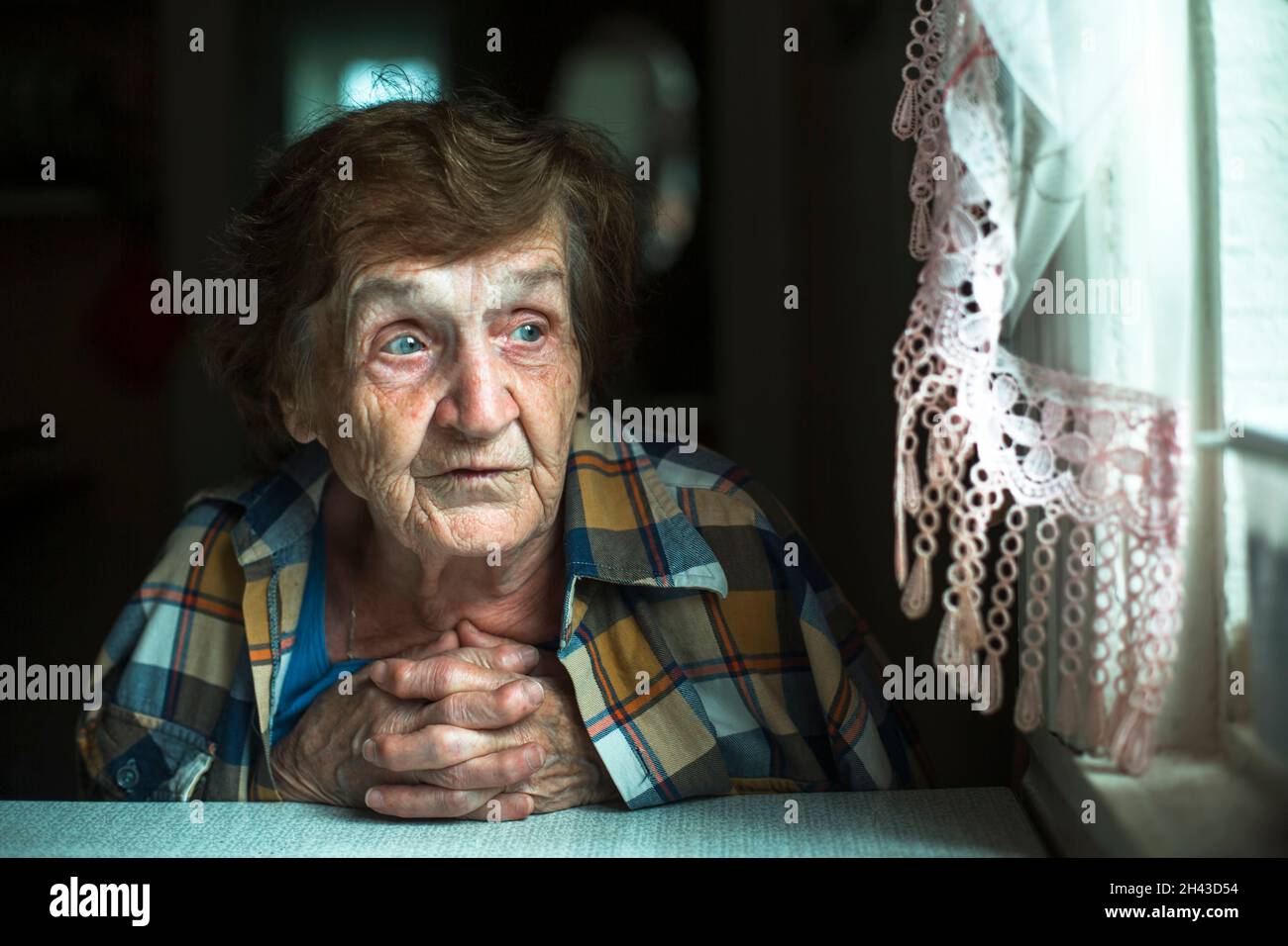 Portrait d'une vieille femme, dans sa maison par la fenêtre. Banque D'Images