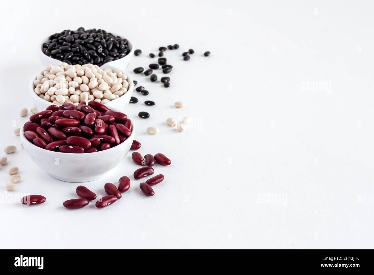 Assortiment de haricots dans un bol blanc sur fond blanc.Haricots rouges, haricots blancs et haricots noirs Banque D'Images