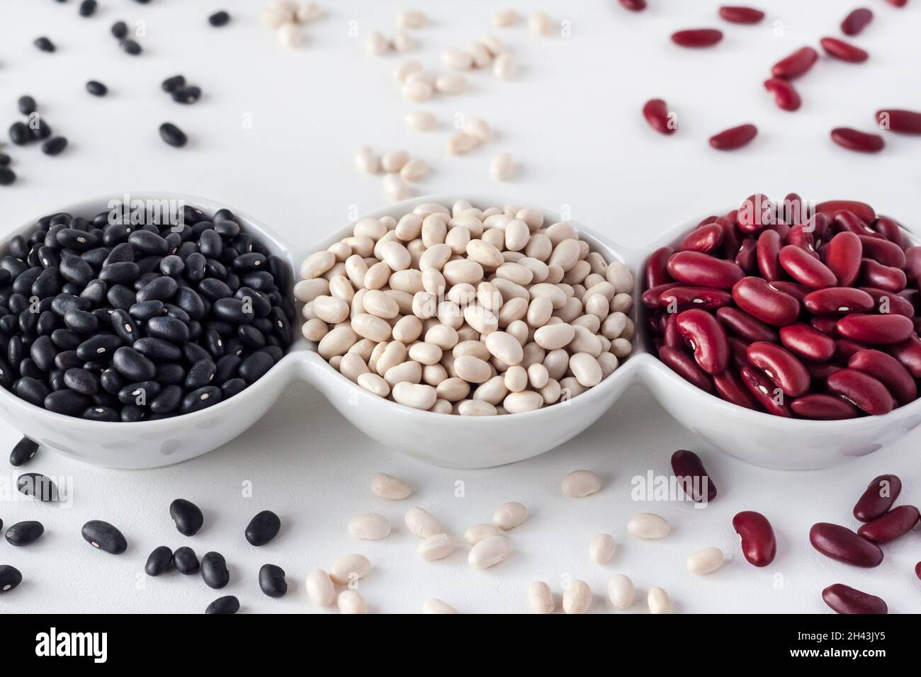 Assortiment de haricots dans un bol blanc sur fond blanc.Haricots rouges, haricots blancs et haricots noirs Banque D'Images