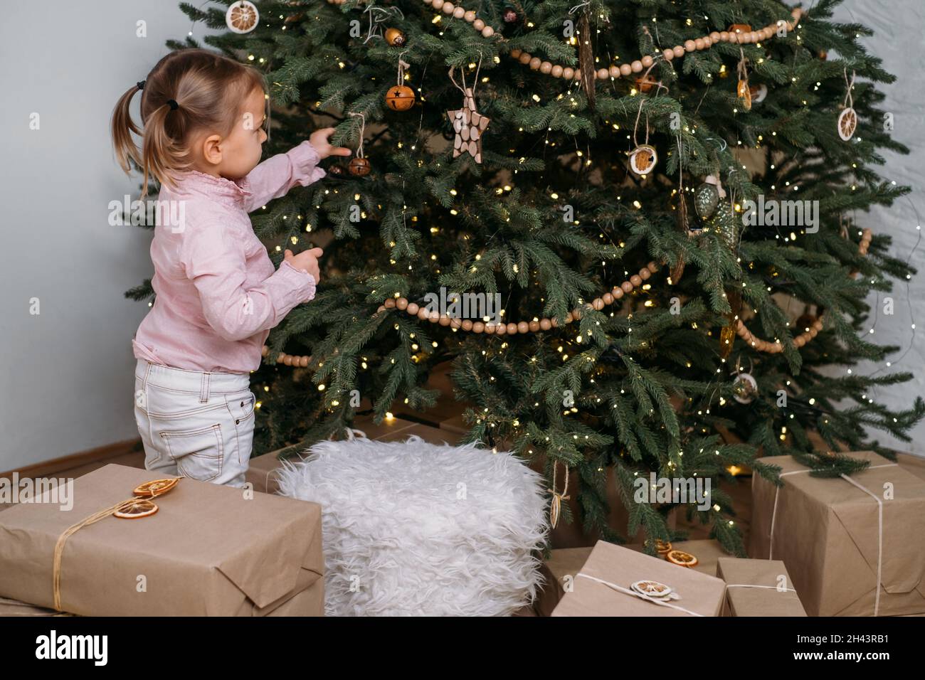 Un enfant adorable attend des cadeaux à la maison après avoir décoré l'arbre de Noël dans un style écologique avec des jouets en bois.Soirée de Noël pour les enfants.Style nordique Banque D'Images