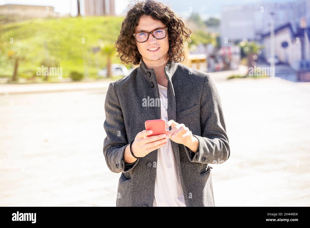 Homme de cheveux longs marchant et utilisant un smartphone Banque D'Images