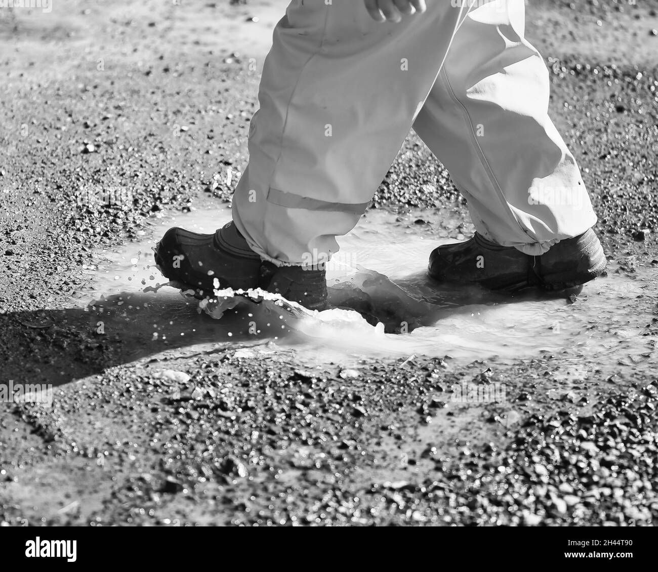 Photo en niveaux de gris d'un enfant marchant sur un étang de terre à l'extérieur sous la lumière du soleil Banque D'Images