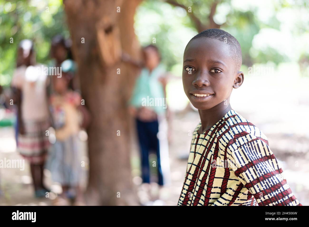 Portrait d'un adorable garçon africain noir aux cheveux fraîchement rasés, souriant à l'appareil photo, avec un groupe d'enfants en arrière-plan Banque D'Images