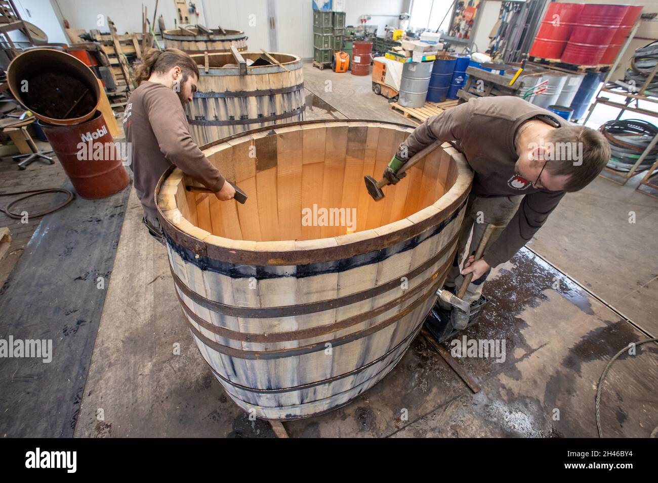 PRODUCTION - 11 octobre 2021, Bavière, Eußenheim: Les vibrateurs Frederik Zink (l) et Wolfgang Rüth de l'atelier vibratoire Aßmann entraînent les cerceaux de tonneau (anneaux de fer) sur les barres de tonneau avec un marteau.Photo: Daniel Karmann/dpa Banque D'Images