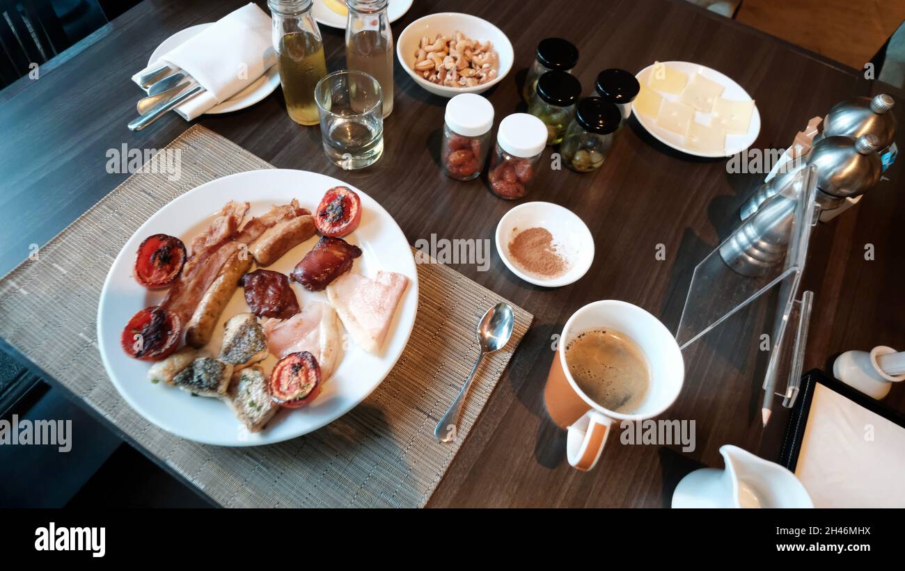 Petit déjeuner complet avec bacon, saucisses de porc, poisson, noix, tomates, olives, café,Jus de pomme, repas du matin Banque D'Images