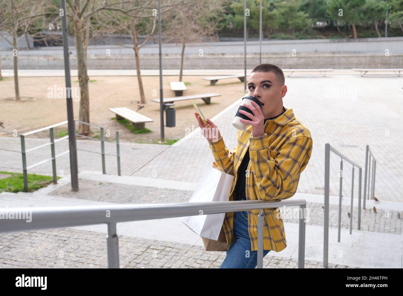 Jeune homme avec maquillage sur boire du café et tenir des sacs de shopping. Banque D'Images