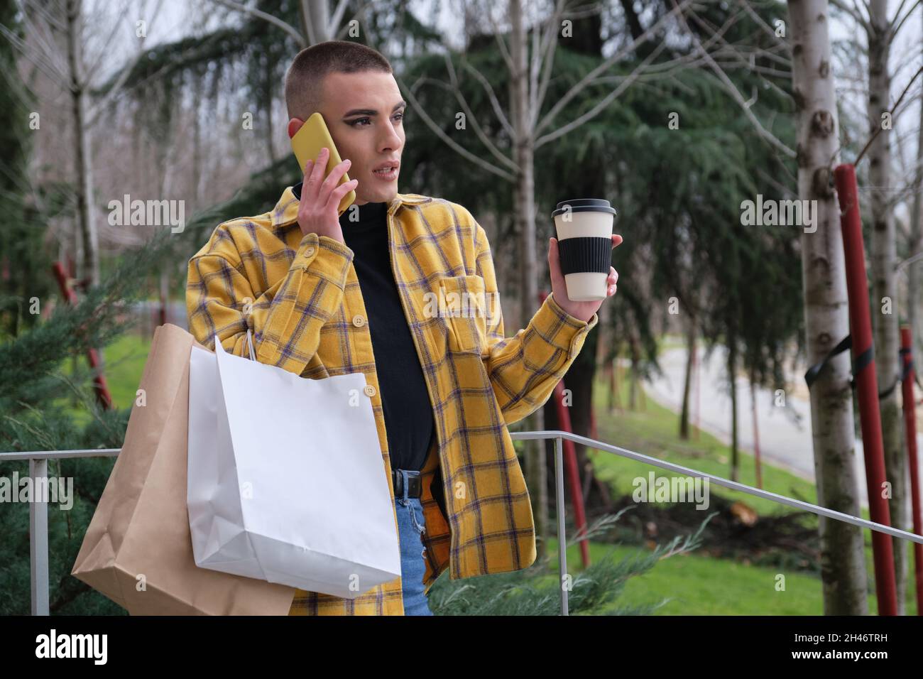 Jeune homme avec maquillage parler sur le smartphone avec des sacs d'achats. Banque D'Images