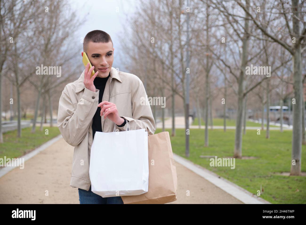 Jeune homme portant un maquillage tenant des sacs d'achats et parlant sur un smartphone. Banque D'Images