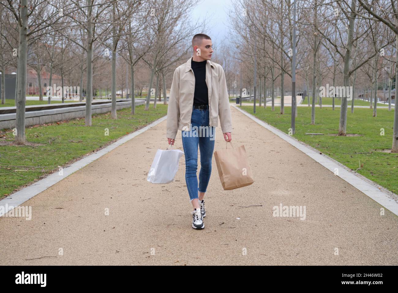 Un jeune homme portant du maquillage marche avec des sacs de shopping et de la musique. Banque D'Images