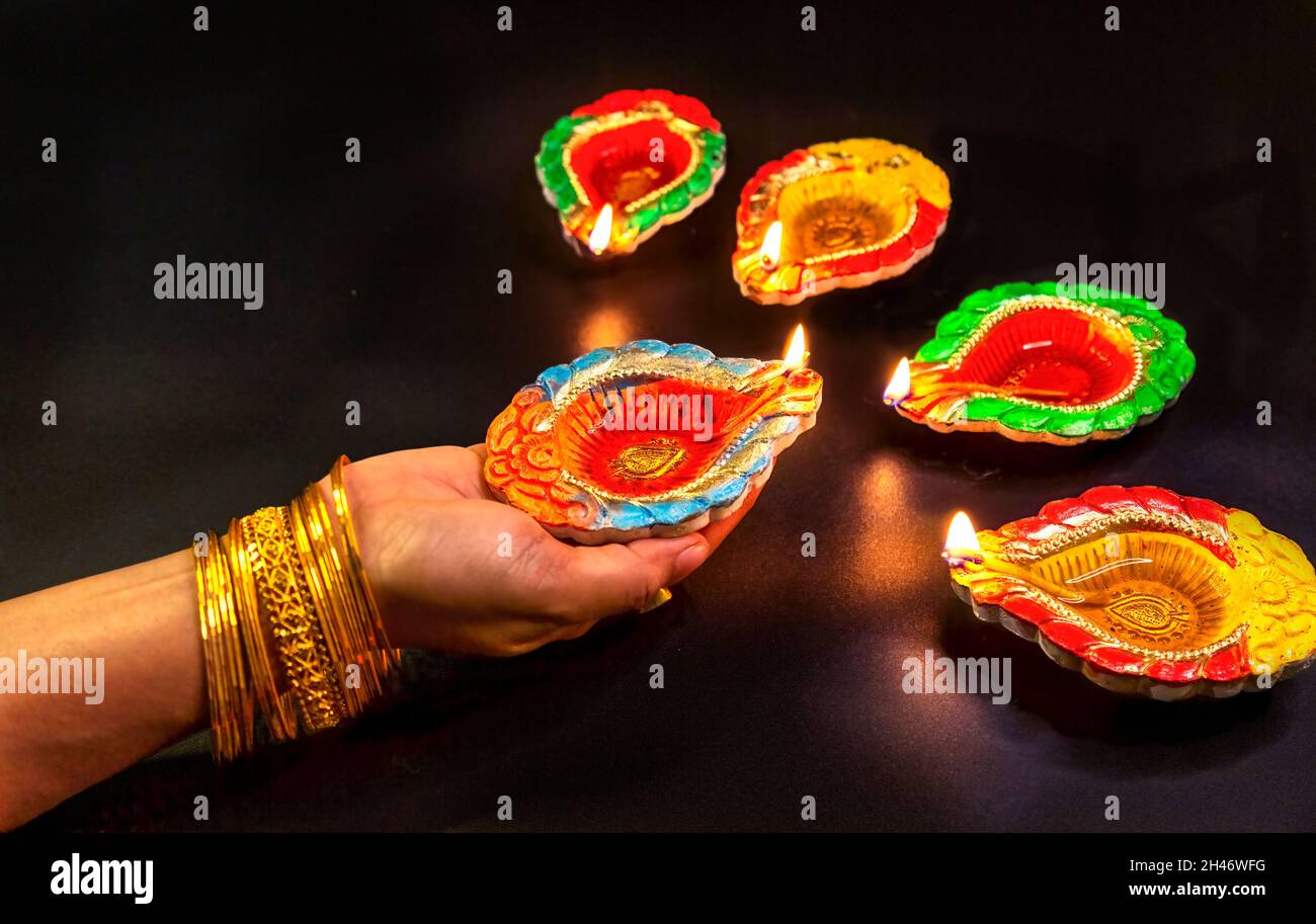 Femme porte main mehndi et bangles éclairant les lampes Diwali Diya sur fond sombre Banque D'Images