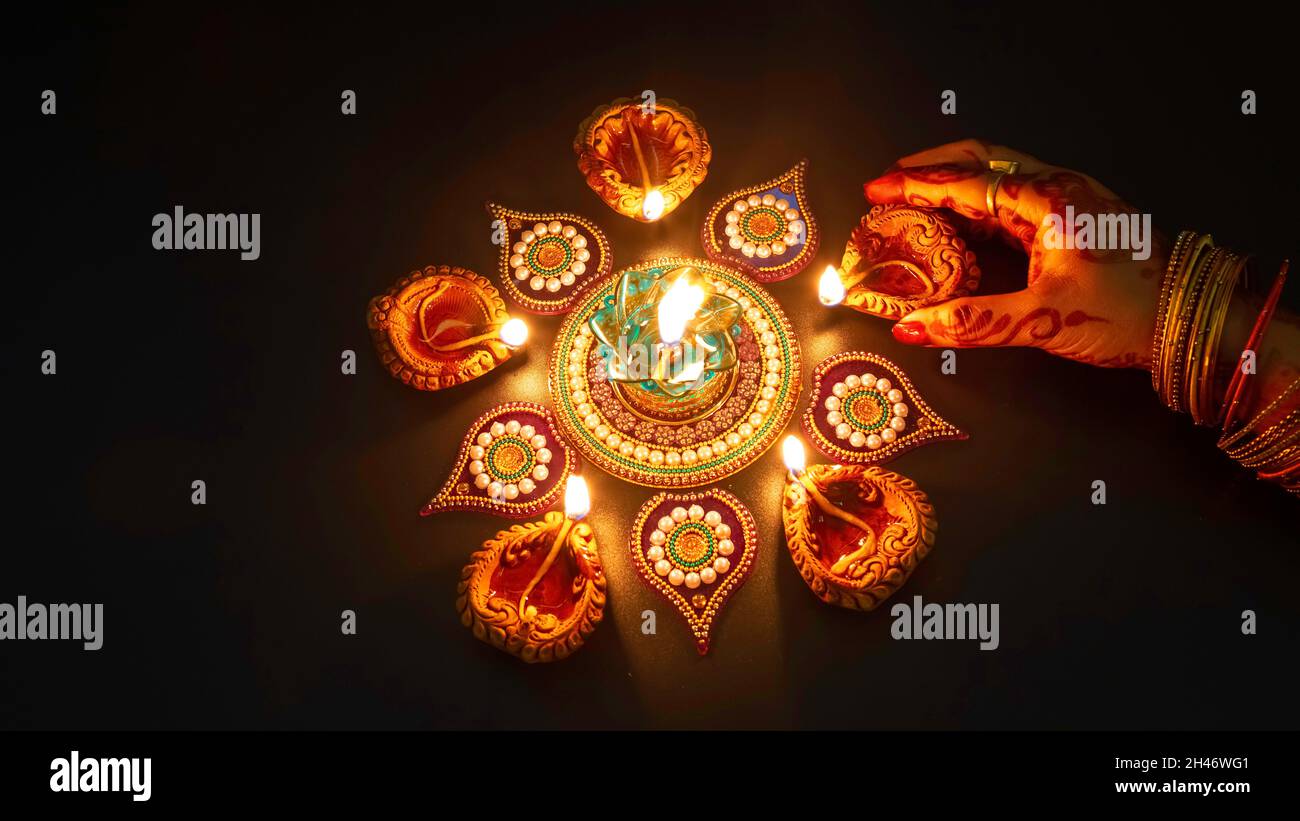 Femme porte main mehndi et bangles éclairant les lampes Diwali Diya sur fond sombre Banque D'Images