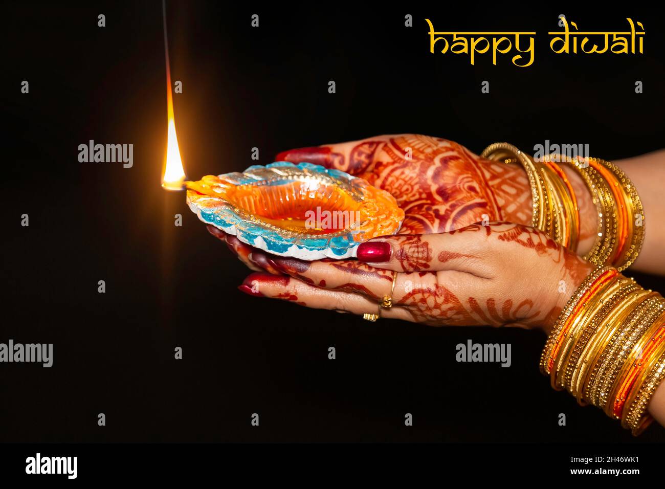 Femme main portant mehndi et bracelets en gros plan tenant une lampe Diwali Diya dans un fond sombre Banque D'Images