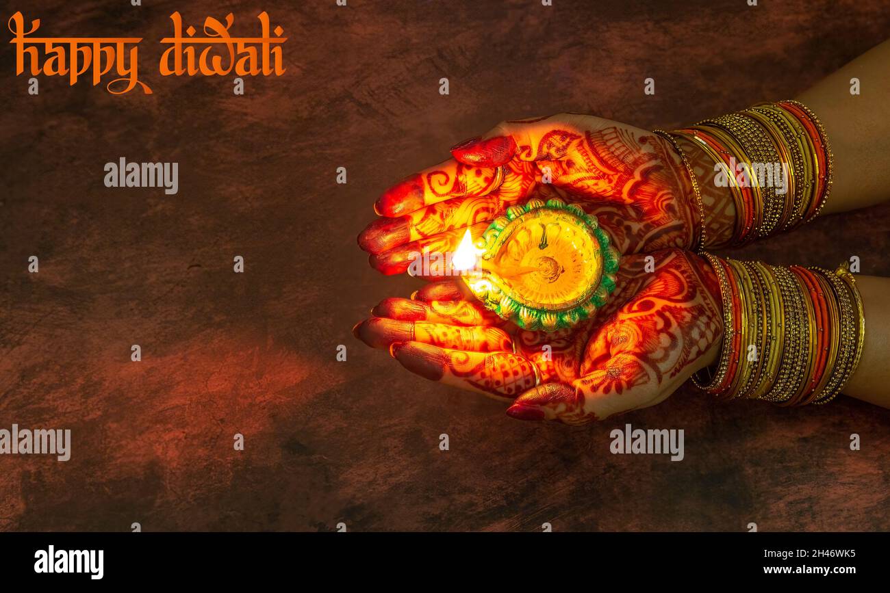 Femme main portant mehndi et bracelets en gros plan tenant une lampe Diwali Diya dans un fond sombre Banque D'Images
