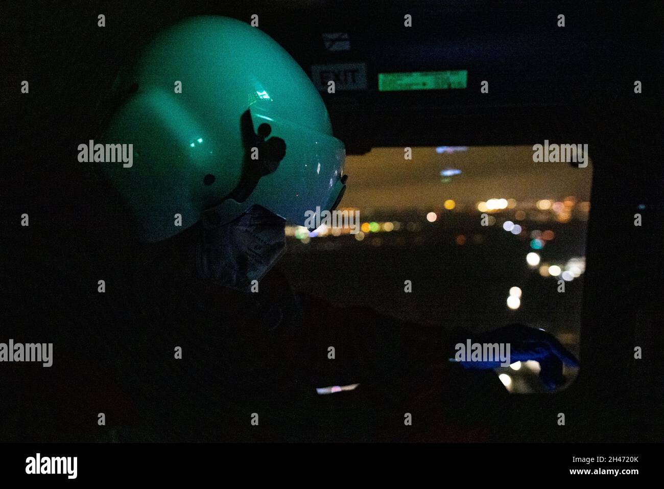 PRODUCTION - 11 octobre 2021, Bade-Wurtemberg, Stuttgart :Le médecin urgentiste, le Dr Christoph Herzog, surveille les signes vitaux de son patient sur un écran pendant le vol vers un hôpital, tandis que son casque est éclairé en vert par le panneau de commande au-dessus de lui et que les lumières de la ville sont visibles par la fenêtre en arrière-plan.L'hélicoptère de sauvetage Christoph 54 est le seul à Baden-Württemberg à avoir des capacités de vol de nuit.L'équipage de nuit avec les deux pilotes prend le contrôle de l'unité de soins intensifs volante de 6.30 h le soir à 7 h le lendemain matin.Il est stationné Banque D'Images