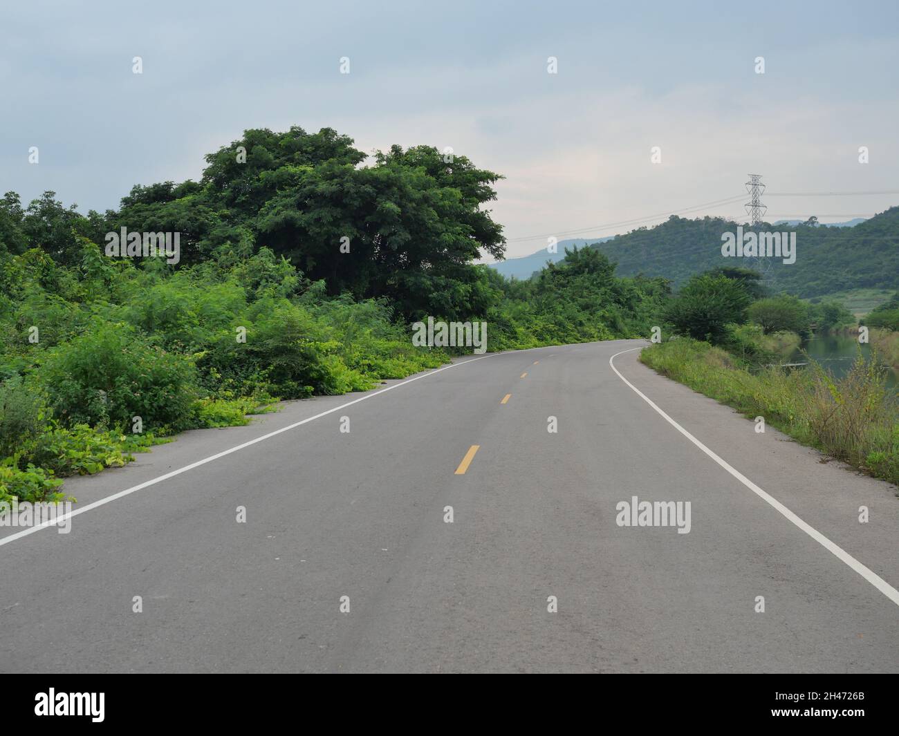 Système d'irrigation et de transport, route asphaltée à courbe ouverte le long du canal avec tour de montagne et haute tension en Thaïlande Banque D'Images