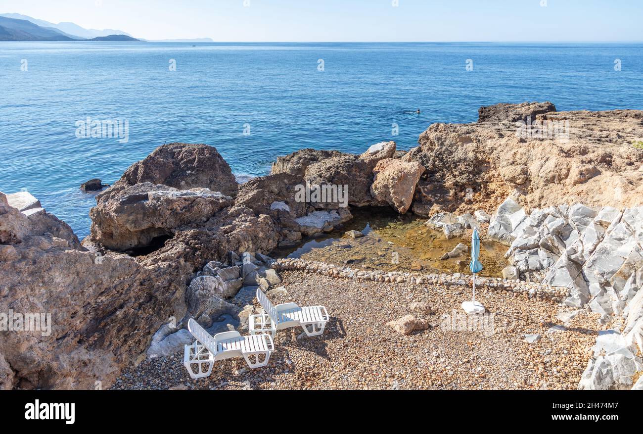 Vacances d'été en Grèce à côté de bleu Egée mer calme fond.Plage rocheuse déserte et vide avec deux chaises longues et un parasol.Plage en plastique blanc ch Banque D'Images
