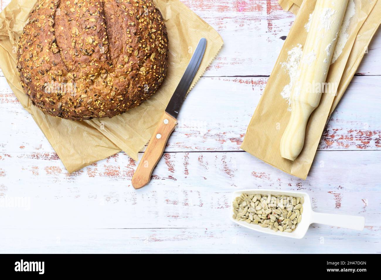 Vue de dessus de pain de seigle sur une serviette sur un fond rustique en bois avec des graines, un couteau, et un rouleau Banque D'Images