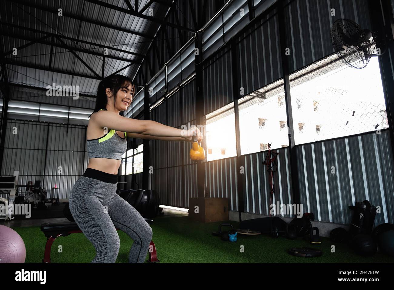 Les jeunes femmes asiatiques aiment faire de l'exercice avec une cloche de bouilloire de levage d'une main à la salle de gym. Concept de culturisme de sport. Banque D'Images